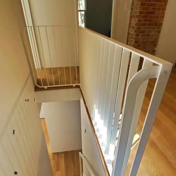 Side view of a white railing set down a staircase.  Curved ends on all corners and the grab rail make this low gloss white railing unique to this craftsman's house turned modern.