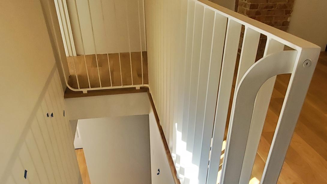 Side view of a white railing set down a staircase.  Curved ends on all corners and the grab rail make this low gloss white railing unique to this craftsman's house turned modern.