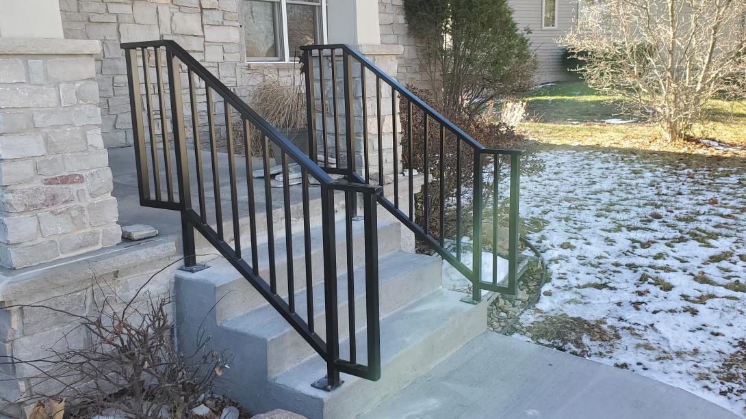 Two black modern craftsman railings sit on both sides of this stoop. 